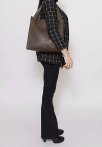 Sacoche en cuir marron avec deux courtes poignées, de forme rectangulaire, surface texturée et design minimaliste. Aucun matériel ou motif visible.