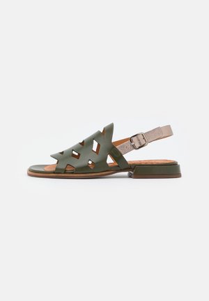 Sandalo flat in pelle verde con ritagli geometrici, cinturino beige regolabile alla caviglia con fibbia argento e tacco basso impilato.