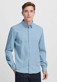 Camisa de manga larga azul claro con cuello abotonado. Presenta una textura suave y un cierre de botón estándar en la parte delantera.