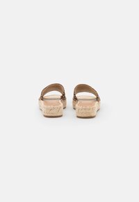 Brown woven sandals with a natural rope platform, open back, and flat sole. Features a textured strap with a subtle pattern.