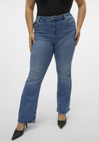 Blue denim jeans with a straight-leg cut, five-pocket design, and a button-fly closure. Paired with black, pointed-toe heels.