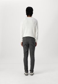 White ribbed sweater, gray tailored pants, and black sneakers. The outfit is viewed from the back against a plain background.
