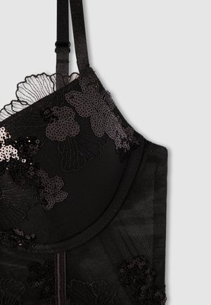 Reggiseno nero con motivi in pizzo floreale e paillettes, spalline regolabili e una texture liscia. I dettagli includono bordi ondulati e un design strutturato.