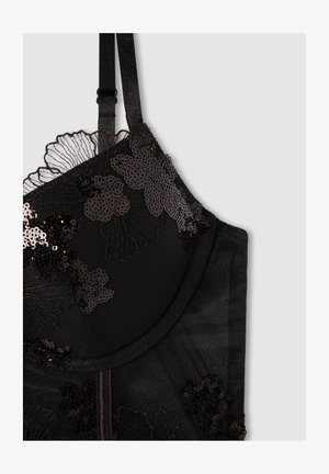 Reggiseno nero con motivi in pizzo floreale e paillettes, spalline regolabili e una texture liscia. I dettagli includono bordi ondulati e un design strutturato.
