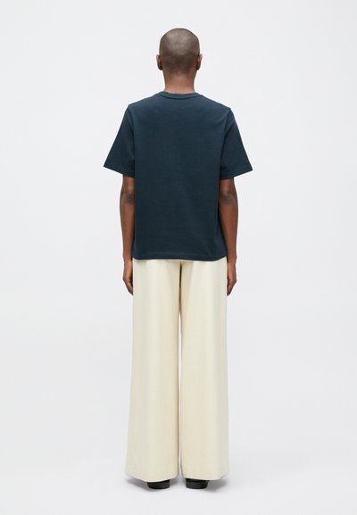 Námořnická bavlněná trička s krátkým rukávem a kulatým výstřihem, spárovaná s krémovými kalhotami se širokými nohavicemi. Hladká textura a uvolněný střih.