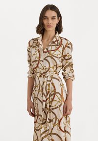 Abito camicia a maniche lunghe in tessuto crema con un motivo a catena dorato e rosso, con apertura frontale a bottoni e una cintura annodata in vita.