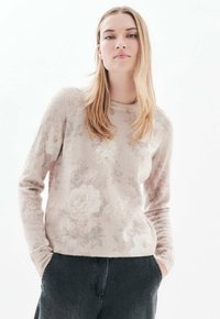 Vaaleanpunainen neulepaita, jossa on kukkakuosi, valmistettu pehmeästä materiaalista. Sisältää pyöreän kaula-aukon ja pitkät hihat, yhdistetty tummiin housuihin.