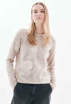 Lichtroze sweater met een bloemenpatroon, gemaakt van zacht materiaal. Heeft een ronde hals en lange mouwen, gecombineerd met donkere broek.