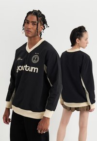 Jersey negro de mangas largas con cuello en v beige, paneles de manga en contraste y texto de logo en el frente; diseño de ajuste holgado.