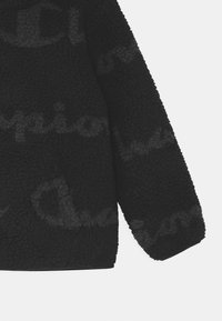 Giacca in pile nera con superficie testurizzata, caratterizzata da un sottile motivo ripetuto del logo "Champion". Include una tasca frontale e una vestibilità ampia.