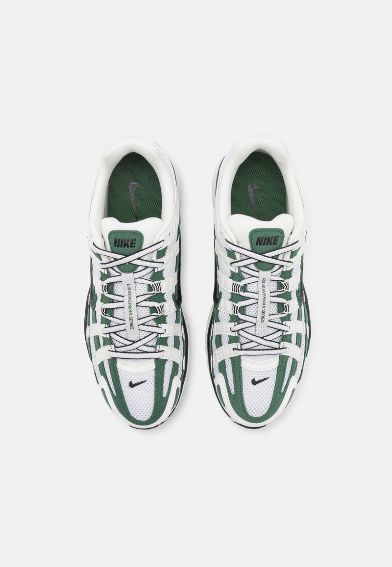 Baskets Nike avec une tige en maille blanche et des accents verts, un système de laçage complexe, un col rembourré et un logo noir sur l'avant.