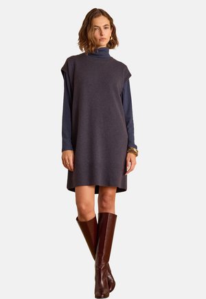 Knit dress in dark gray with a high neck, short sleeves, ribbed hem, worn over a navy long-sleeve top, paired with brown knee-high boots.