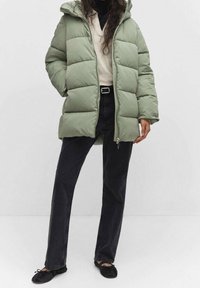 Steppjacke in Hellgrün mit Reißverschluss und Kapuze. Kombiniert mit schwarzen, weitgeschnittenen Jeans und schwarzen Slippern.