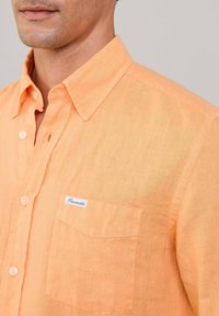 Lichtoranje overhemd met knopen, gemaakt van linnen, met een kraag, een zak op de linkerborst en een label met "Faconnable" branding.
