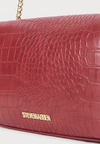 Bolso de mano rojo con textura de cocodrilo y cadena dorada, con el logotipo dorado "STEVE MADDEN" en la tapa frontal.
