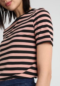 Rosa och svart randig t-shirt med kort ärm, rundad halsringning, ribbad textur och synliga sömmar längs ärmarna.