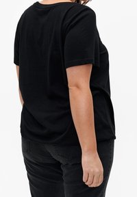 Sort bomuld t-shirt med korte ærmer, rund halsudskæring og afslappet pasform. Sammen med sorte jeans, set fra ryggen. Simpelt design.