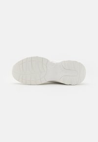 Semelle de chaussure de sport blanche arborant un motif texturé avec des rainures et des crampons pour une meilleure adhérence. Partie supérieure lisse avec des détails de logo.