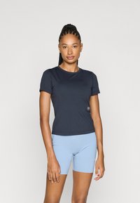 Mørk marineblå kortermet treningsgenser laget av glatt stoff, kombinert med lyseblåt tettsittende shorts. Har en liten logo på framsiden av toppen.