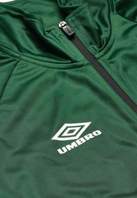 Green athletic jacket made of smooth fabric, featuring a black zipper and a white "Umbro" logo with a diamond design on the front.