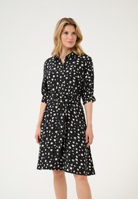 Musta napille kiinnitettävä mekko, jossa on valkoinen abstrakti printti, 3/4 pituiset käännettävät hihat, vyötärönauha ja kellotettu halkio. Valmistettu kevyestä kankaasta.