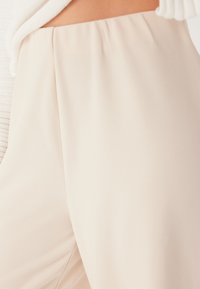 Beige broeken met een gladde textuur en elastische tailleband, met een strak ontwerp en subtiele plooien aan de voorkant.