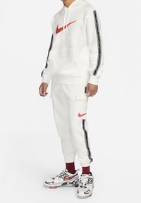 White hoodie with a red Nike logo, matching sweatpants with side stripes, and white sneakers with red accents. Comfortable, casual fit.