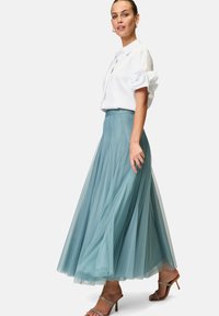 A flowing teal tulle skirt with a fitted waistband, paired with a white blouse featuring puffed sleeves and a button-down design.