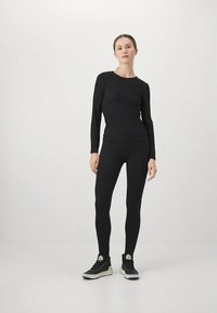 Μαύρο μακρυμάνικο πάνω μέρος και κολάν από ελαστικό ύφασμα, εφαρμοστό σχέδιο, λεία υφή, συνδυασμένα με μαύρα αθλητικά παπούτσια με λευκή λεπτομέρεια.