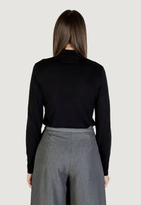 Czarny sweter z długim rękawem i okrągłym dekoltem, zestawiony z szarymi spodniami o wysokim stanie z plisowanym wzorem i gładką teksturą.