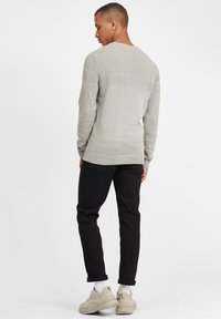 Hellgrauer Strickpullover mit strukturierten Akzenten, gerippten Bündchen und Saum, kombiniert mit schwarzen Hosen und beigen Sneakers mit dicker Sohle.