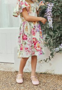 Vestido floral con mangas con volantes en colores pastel, que presenta un corsé ajustado y una falda recogida. Combinado con zapatos Mary Jane en color rosa.