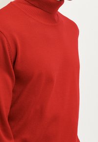Rode coltrui gemaakt van glad, gebreid materiaal, met een aansluitende pasvorm en een getextureerde ribgebreide kraag voor extra warmte.