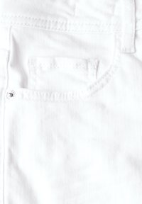 Tela de mezclilla blanca con un pequeño bolsillo frontal, costuras reforzadas y un botón de metal con detalle de logo grabado.