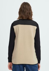 Fleece-Jacke mit einem cremefarbenen und schwarzen Blockdesign, strukturiertem Stoff, langen Ärmeln und einem abgerundeten Saum.
