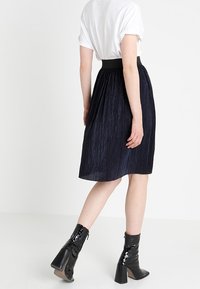Una falda plisada azul marino con una cintura suave, combinada con una camiseta blanca y botas de cuero negro brillante con tacones gruesos.