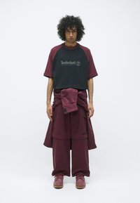 Bordeaux oversized t-shirt met zwarte accenten en logo, gecombineerd met bordeaux cargo pants en bijpassende schoenen, met een ontspannen fit.