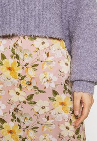 Lila fluffig tröja med ribbade texturer, parat med en rosa blommönstrad kjol som har gula och vita blommor samt gröna blad.