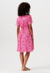Robe à manches courtes en tissu rose à motif floral, cintrée à la taille avec un lien. Comprend une jupe évasée et des sandales unies.