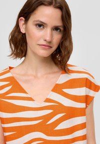 Oranje en crème gestreepte V-hals top met korte mouwen, met een gedurfde zebra print en een lichte stofstructuur.