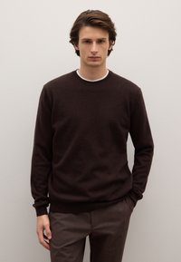 Maglione di lana marrone con scollo rotondo, maniche lunghe e polsini a coste, abbinato a pantaloni marroni. Texture liscia, design minimale.