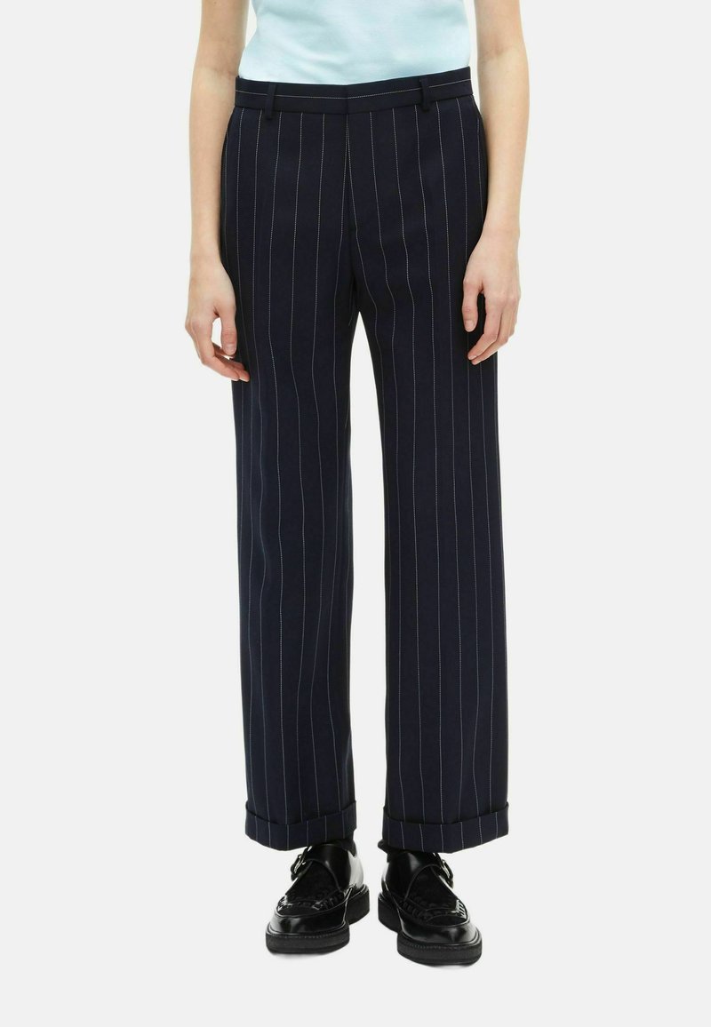 Pantaloni navy a righe con taglio dritto, risvolti, tessuto liscio e design classico. Abbinati a scarpe nere.