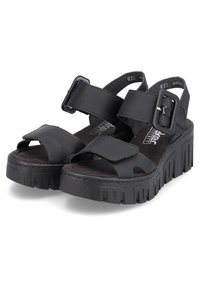 Sandales plateforme noires avec larges sangles, une découpe à l'avant et une boucle. Semelle extérieure texturée avec un motif en relief pour l'adhérence et le soutien.