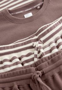 Zwei Loungewear-Stücke: ein geripptes mauvefarbenes Oberteil mit rundem Ausschnitt und ein gestreiftes Oberteil in Weiß und Mauve, kombiniert mit passenden mauvefarbenen Jogginghosen mit Kordelzug.