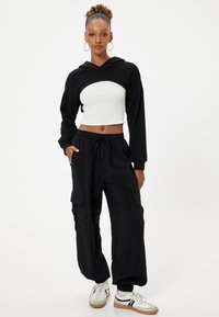 Svart huva crop-top med ett vitt ribbat underlager, parat med lösa svarta cargobyxor med patchfickor och elastiska manschetter.