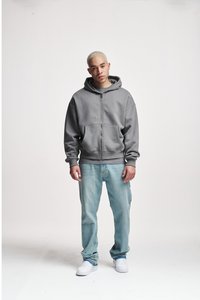 Grau zip-up Kapuzenpullover mit einer Vordertasche, kombiniert mit hellblauen Jeans und weißen Sneakers. Der Stoff wirkt weich mit einer glatten Textur.