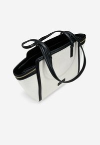 Bolso tote con un cuerpo texturizado en blanco y acentos de cuero negro. Cuenta con dos asas resistentes y un zipper dorado en la parte superior para el cierre.