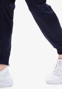 Joggers sportivi blu marino con texture liscia e polsini a costine, abbinati a sneaker bianche con inserti in rete e solidi.