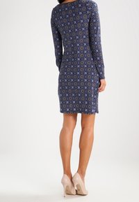 Navy dress with long sleeves, fitted silhouette, and circular pattern. Worn with nude high heels.