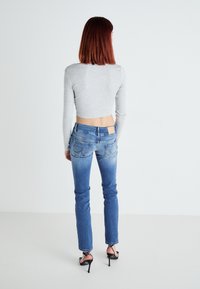 Sivi skraćeni dugi rukav majica u kombinaciji sa plavim skinny trapericama. Traperice imaju svijetli izblijedjeli efekt i svijetlo smeđi zakrpu na stražnjem dijelu struka. Crne sandale na visoku petu.